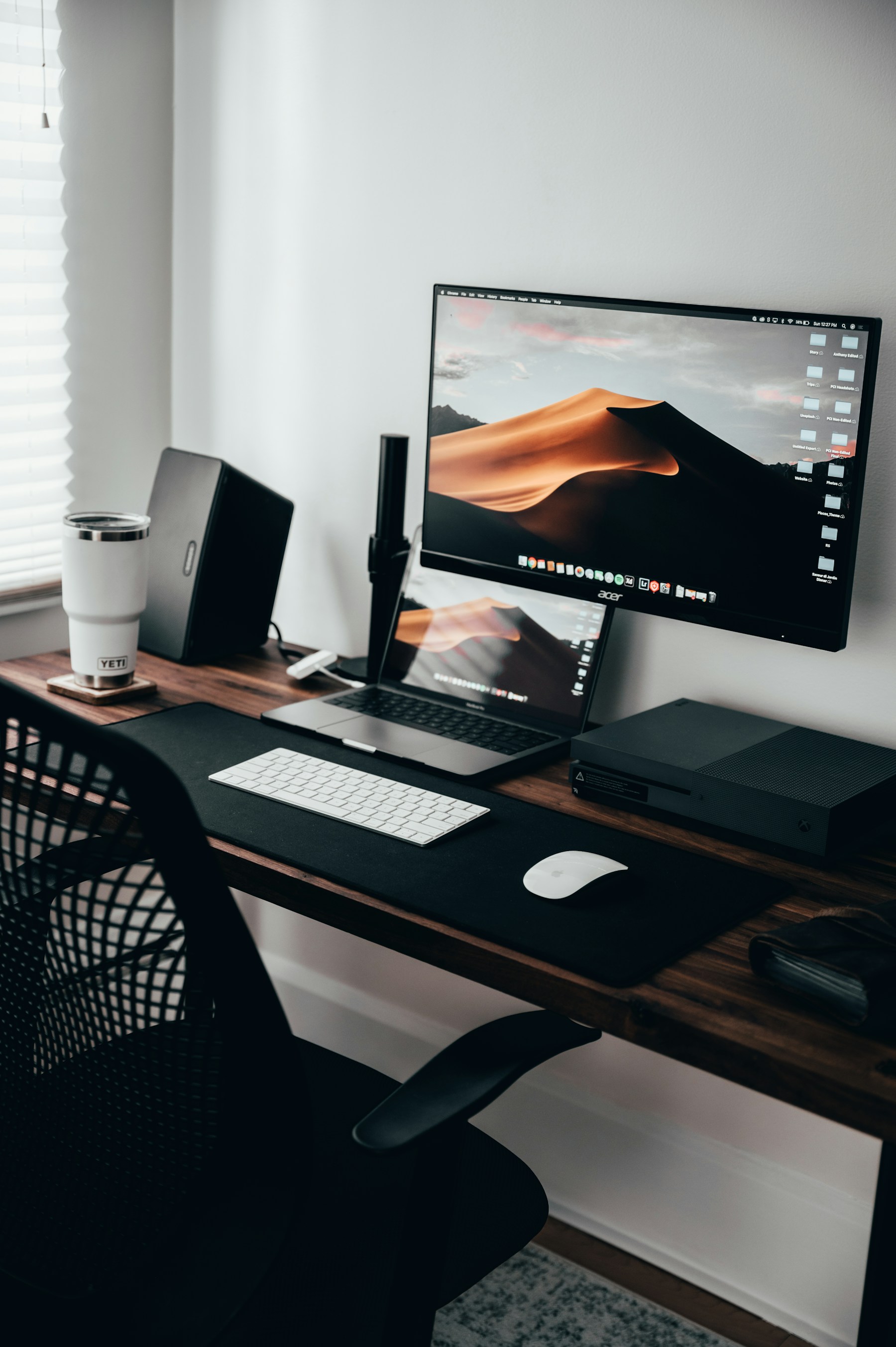 Monitor on a desk mount above a laptop on a wooden desk