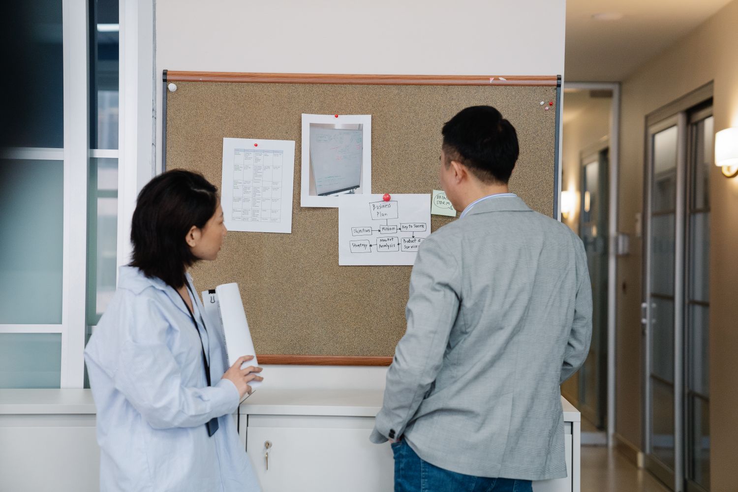 Two people looking at notes on an office pinboard